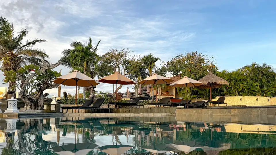 Sunny resort pool in Bali with loungers, umbrellas and reflections on the water