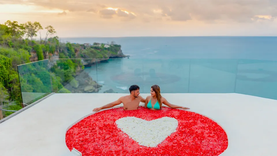Couple in cliffside jacuzzi decorated with heart-shaped flower petals