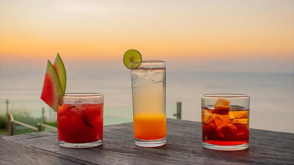 Three sunset cocktails on wooden table overlooking the ocean